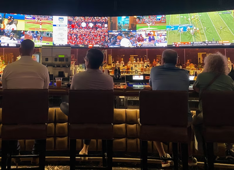 People sitting at a bar with a row of tvs in front of them